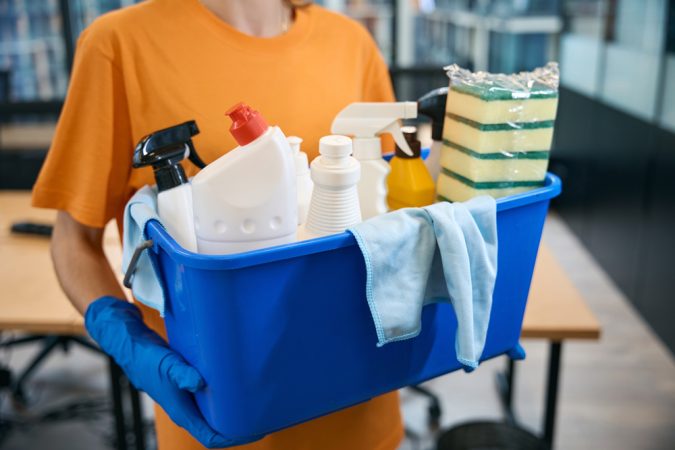 Cleaner cleaning company holds in her hands professional set of gadgets for cleaning and disinfection - bucket, sponges, spray, napkins, detergents
