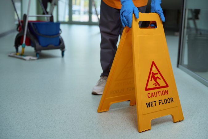 Cropped photo of cleaner in gloves placing a yellow warning sign on the freshly-cleaned floor